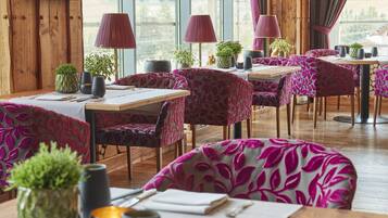 En restaurantindretning med trævægge, borde med stole betrukket med lilla blade, og plantet blomster.