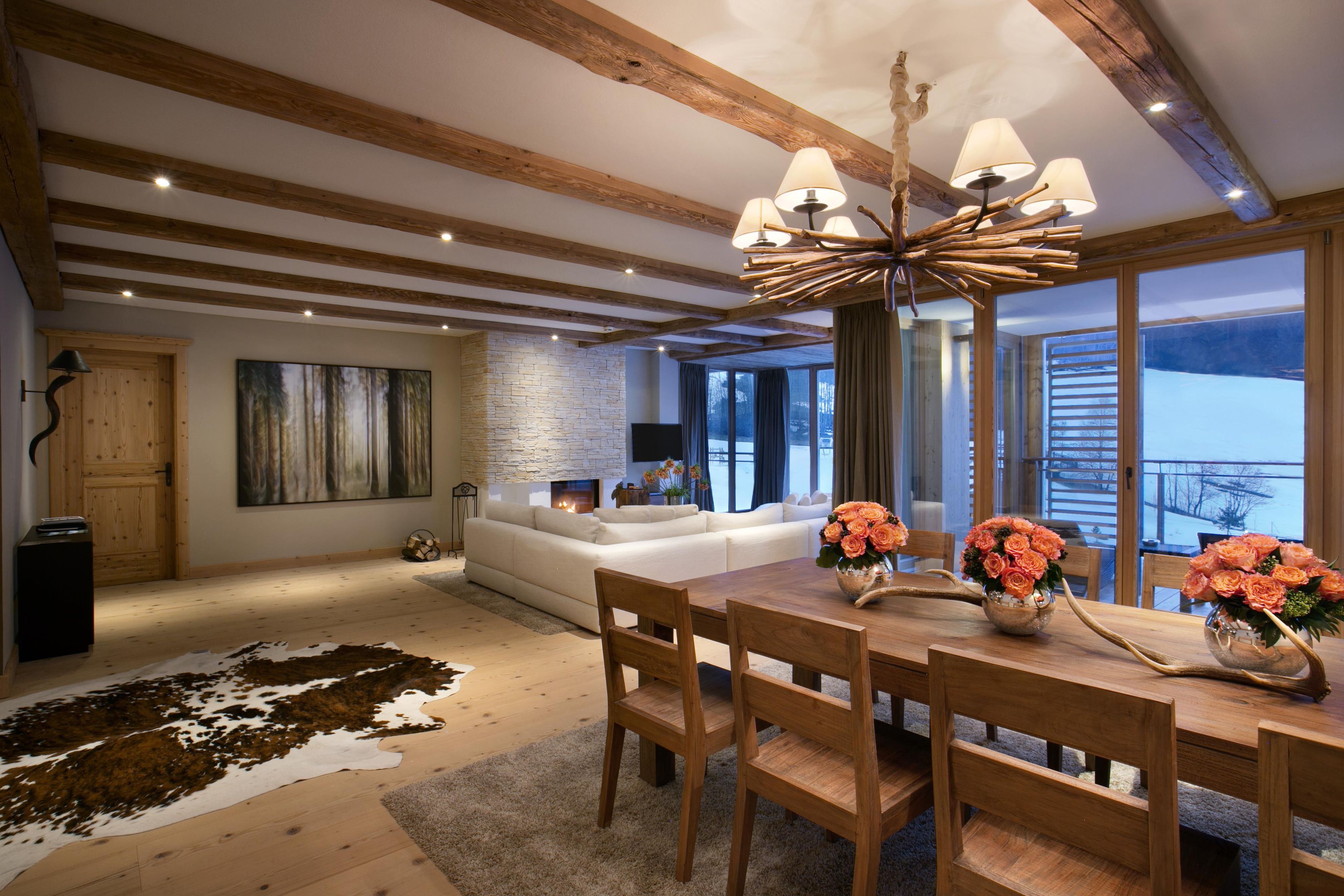 Een ruime woonkamer met een open haard, een eethoek met een houten tafel en stoelen, en grote ramen met uitzicht op het omliggende landschap.