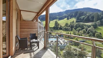 Een houten balkon met glazen hekwerk met uitzicht op een groene vallei en een zwembad.
