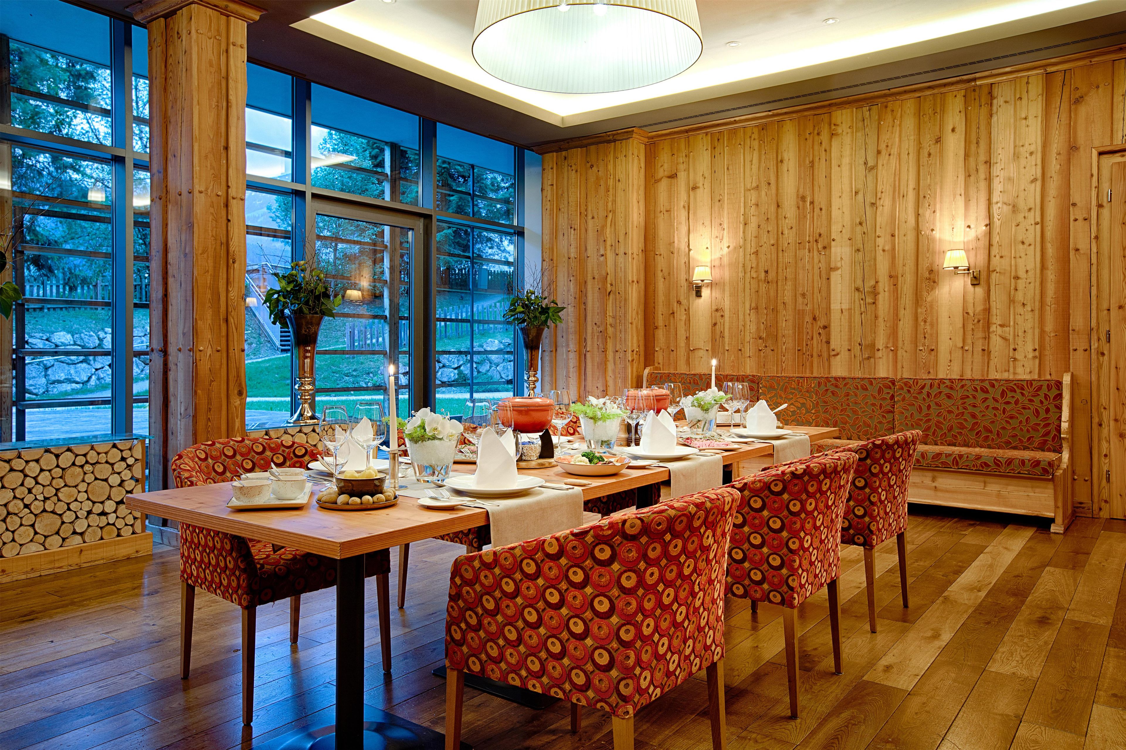 Un espace repas avec une longue table dressée pour le repas, des murs lambrés et de grandes fenêtres offrant une vue sur l’extérieur.