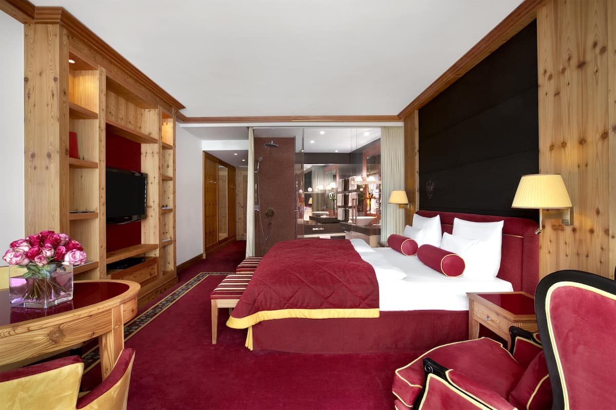 A hotel room with a large bed, wooden furniture, a TV, and a view into the kitchen area.