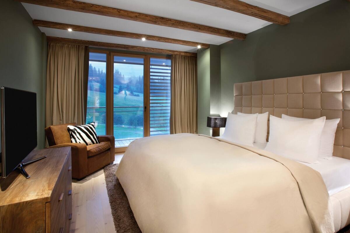 A large bed with a tufted headboard, a wooden nightstand, a TV, and a leather armchair.