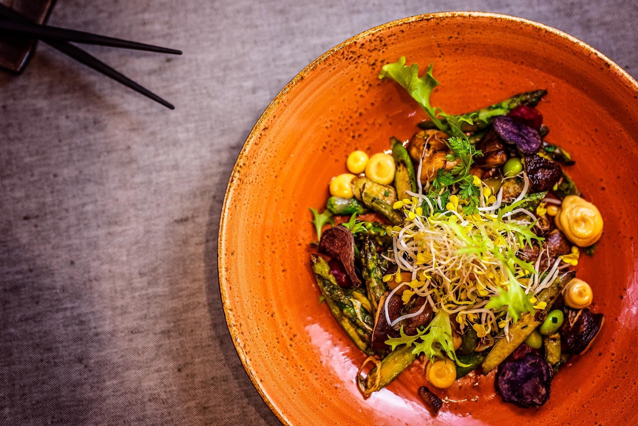 A bowl of salad with various vegetables and sprouts on a textured surface.