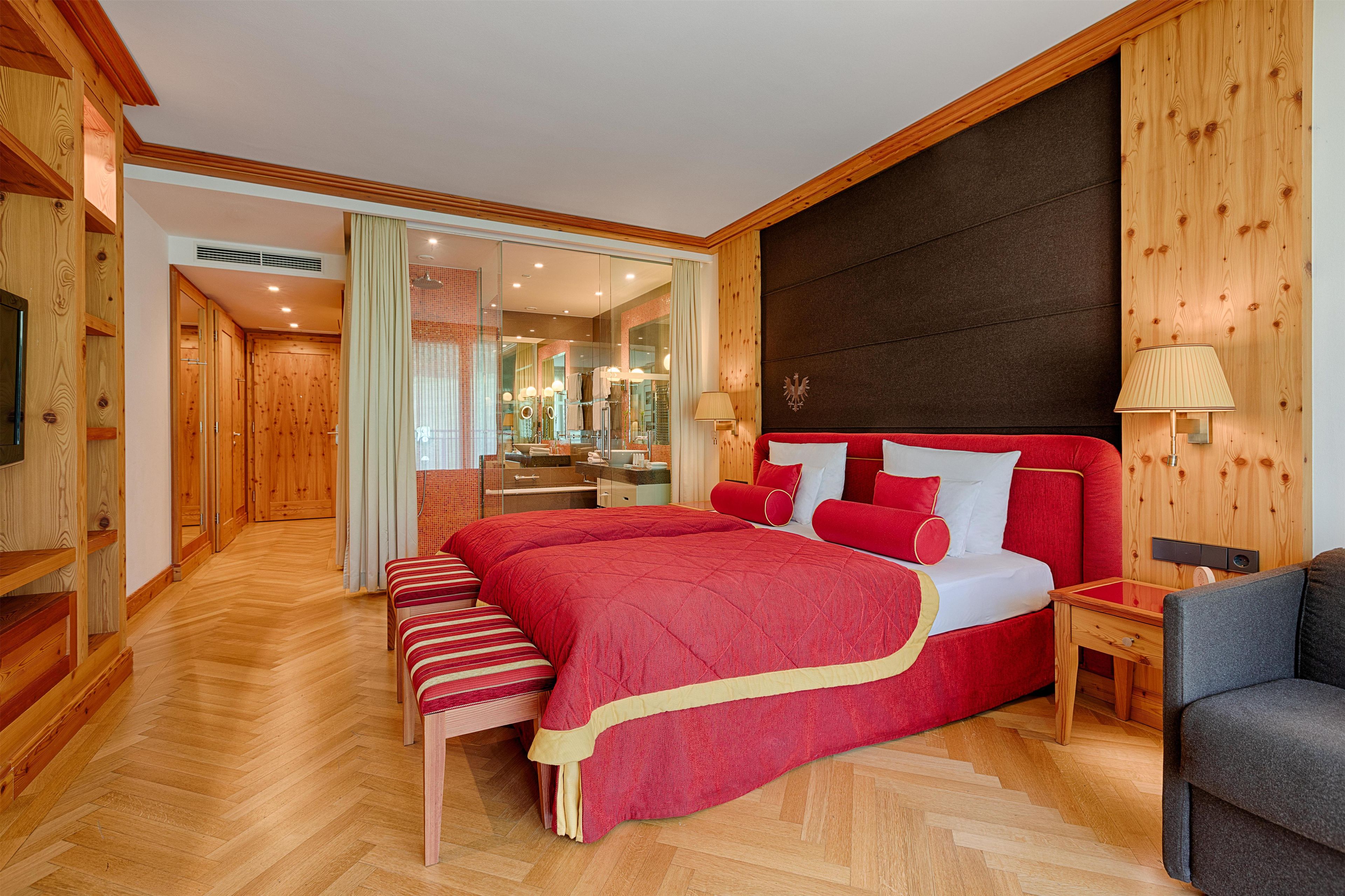 A spacious bedroom with a large bed, wooden paneling, and a modern bathroom visible through a glass door.