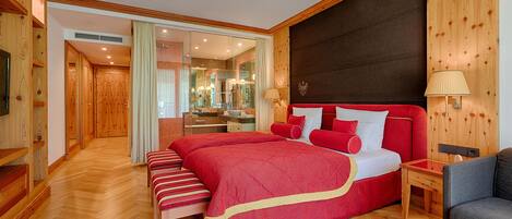 A spacious bedroom with a large bed, wooden paneling, and a modern bathroom visible through a glass door.
