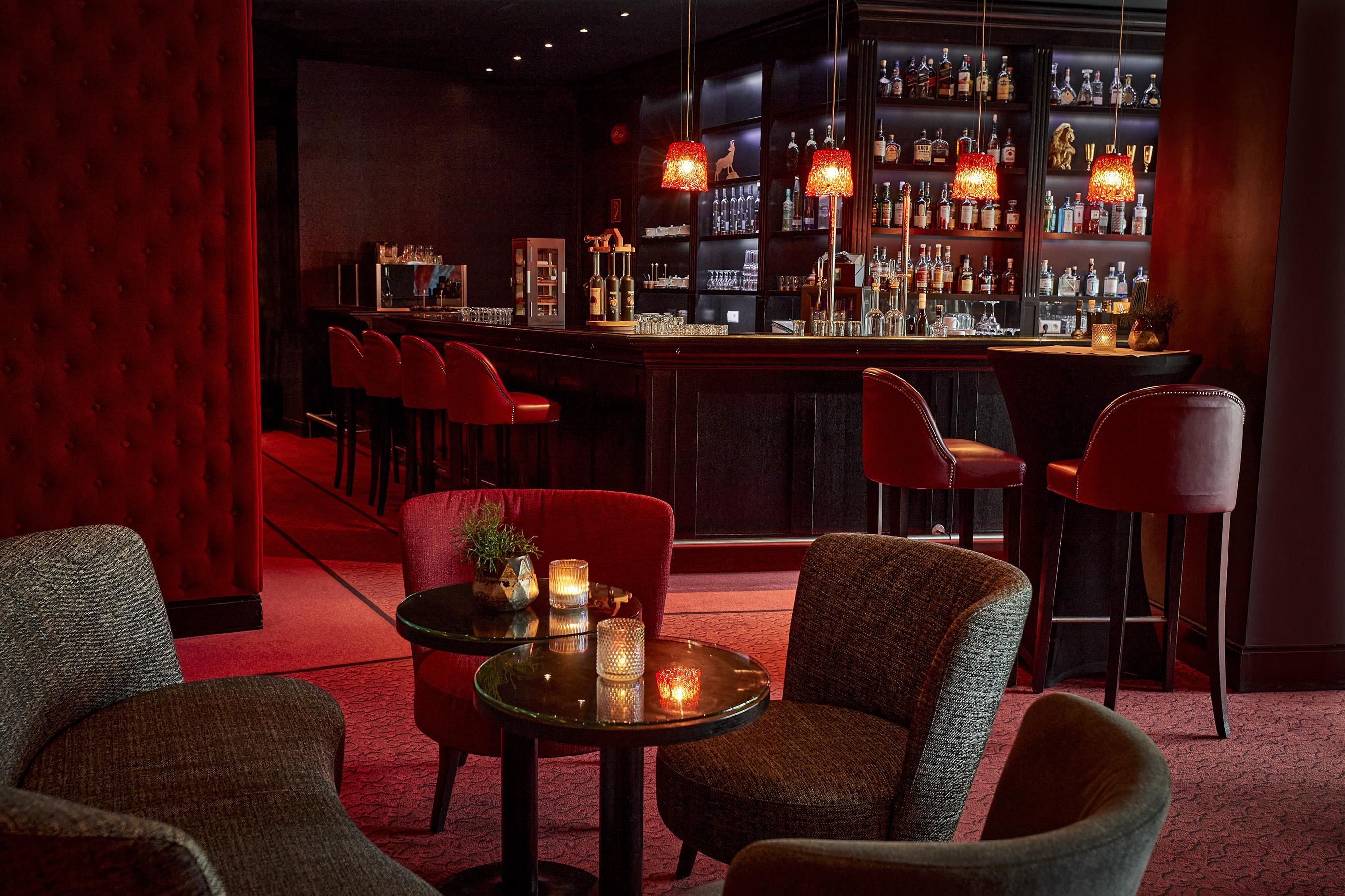 A bar area with red upholstered chairs, a bar counter with various bottles, and a red velvet wall.