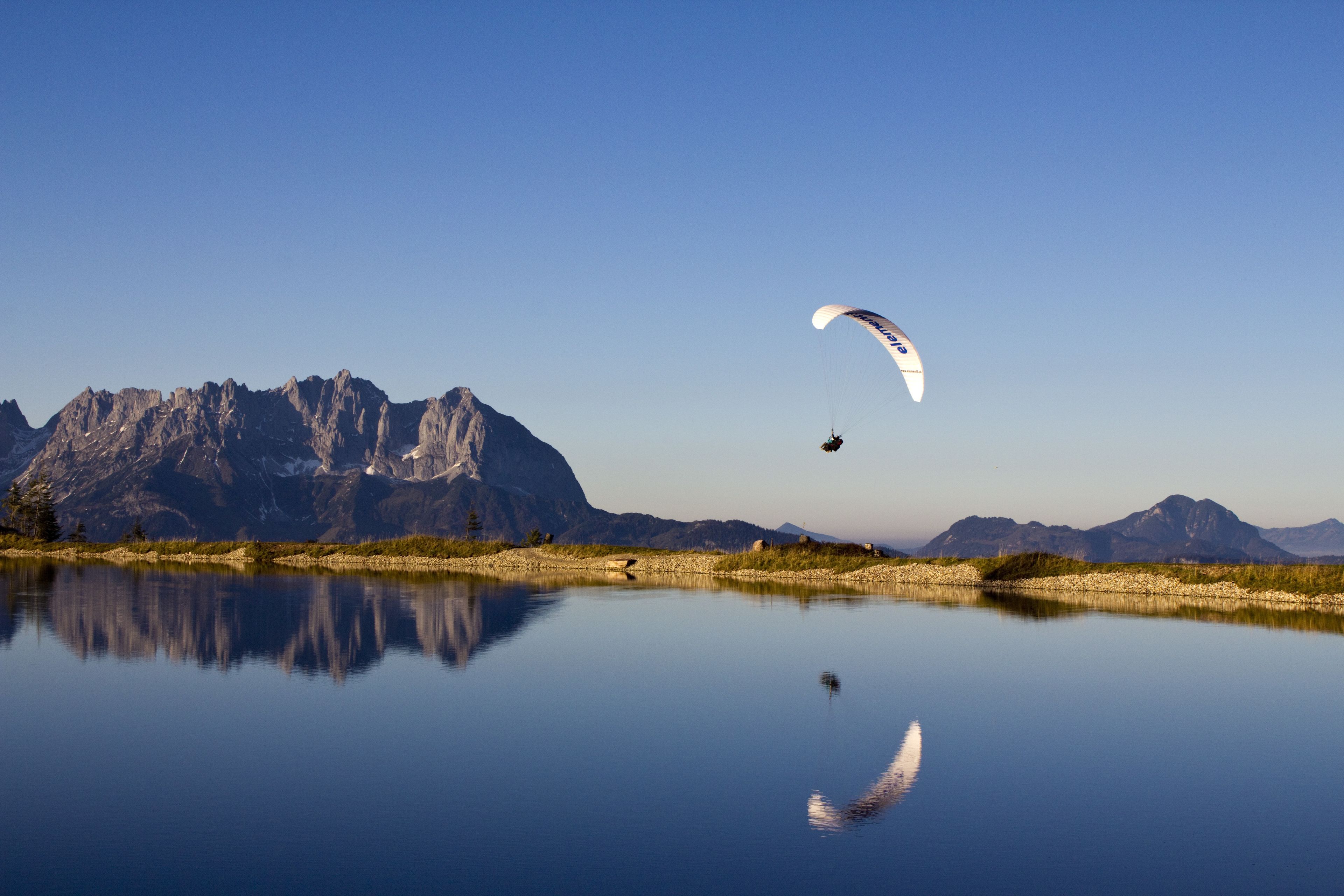 Een paraglider boven een rustig meer, met bergen op de achtergrond.