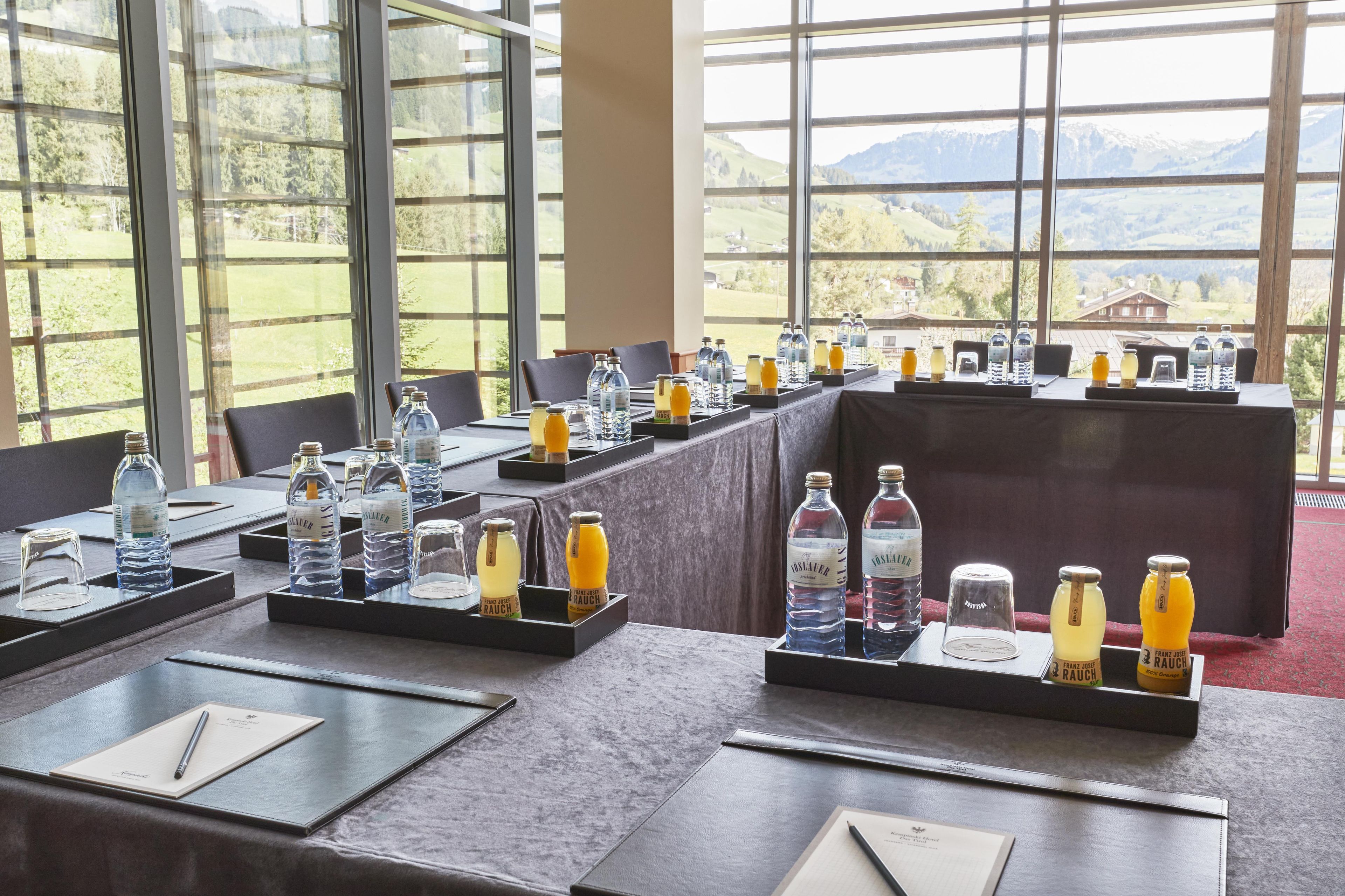 Un salón de conferencias con mesas dispuestas para una reunión, equipado con botellas de agua, vasos y blocs de notas.