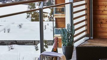 A balcony with a mountain view, a table with glasses and a bottle, and a potted plant.