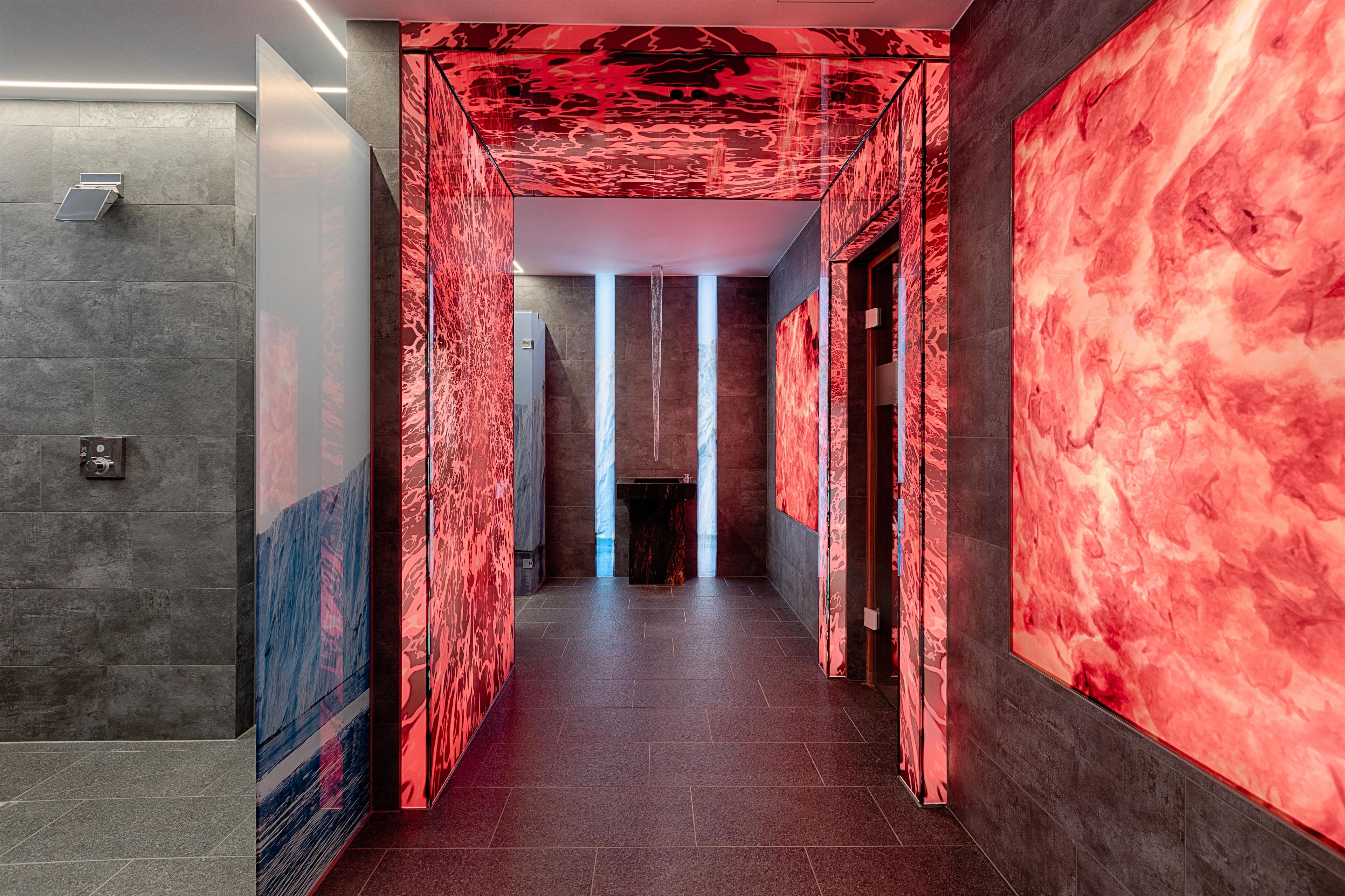 Un pasillo con una pared iluminada en rojo y una textura similar al mármol en el lado derecho.