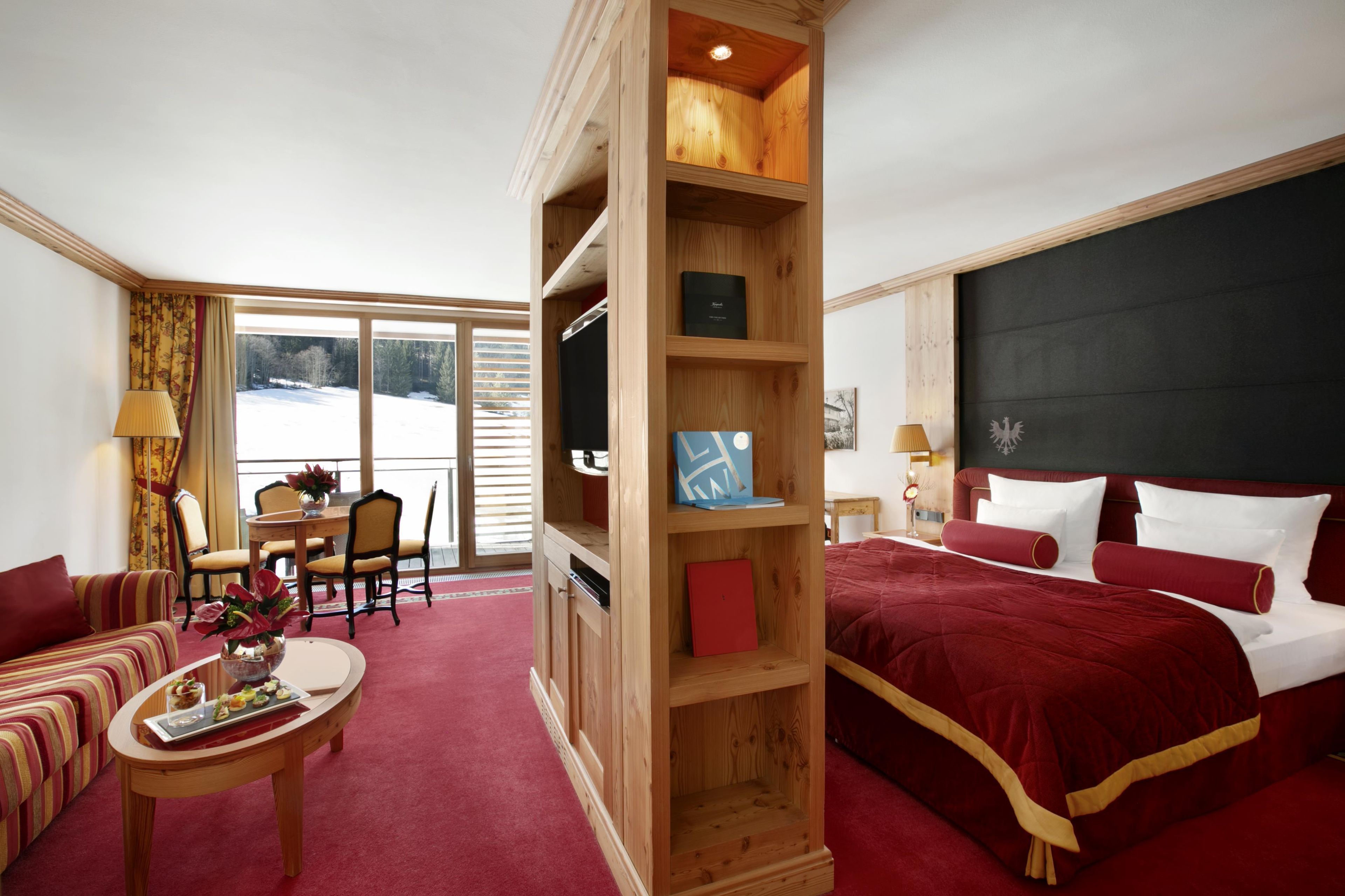 Een hotelkamer met een groot bed, een houten boekenkast, een zithoek met een tafel en stoelen, en uitzicht op de omgeving.