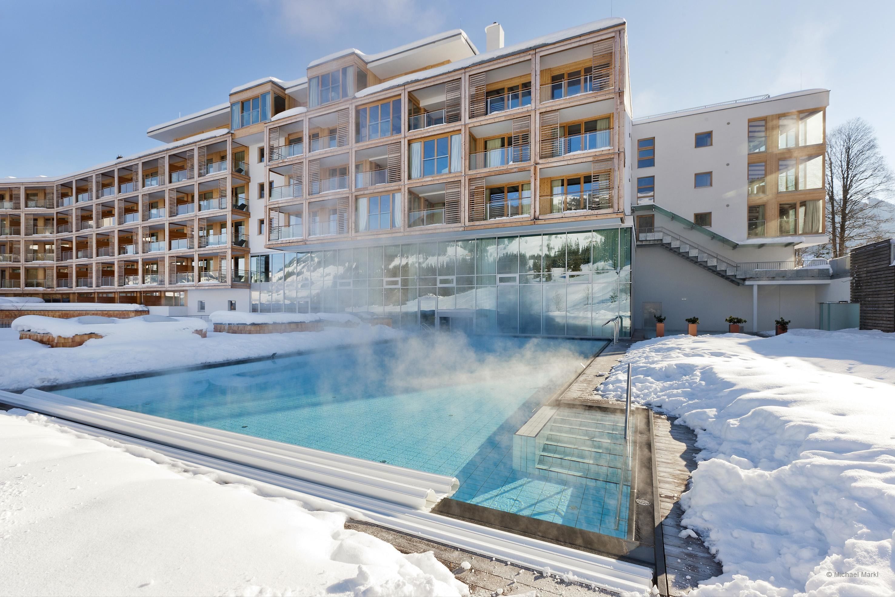 Un hotel moderno con varios balcones, una zona de piscina nevada y cielo despejado.