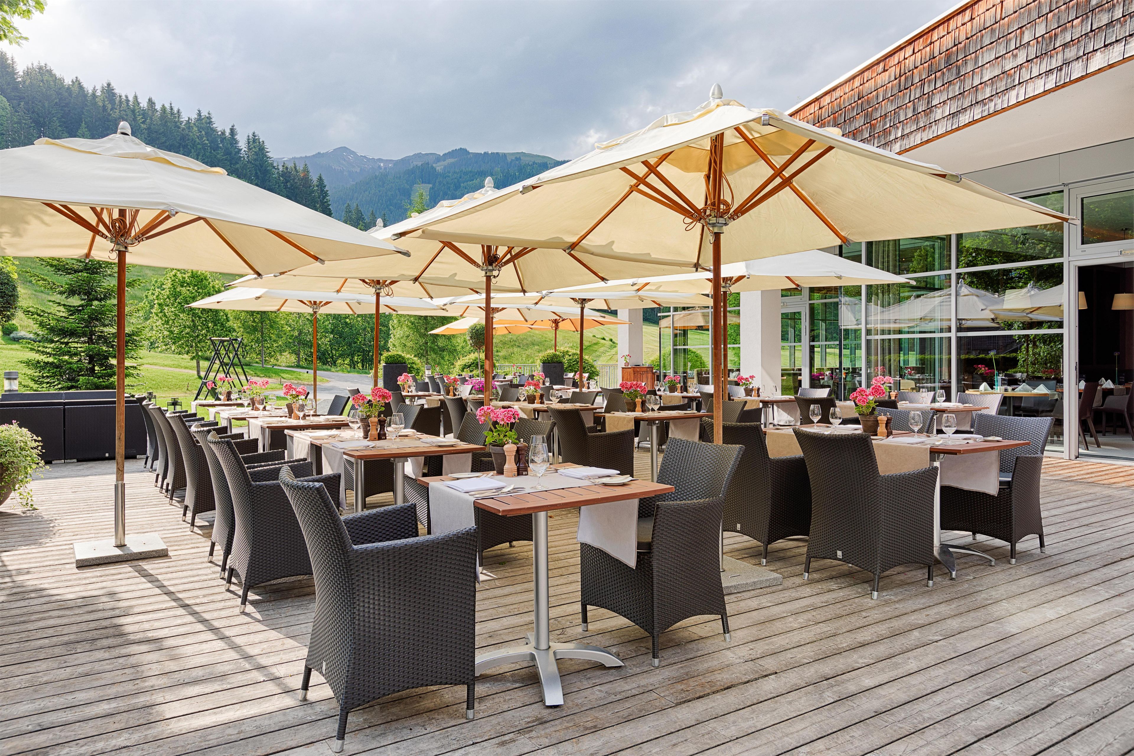 An outdoor dining area with tables and chairs, large umbrellas, and a view of mountains in the background.