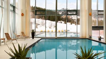 Une piscine intérieure offrant une vue dégagée sur un paysage enneigé grâce à de grandes fenêtres.