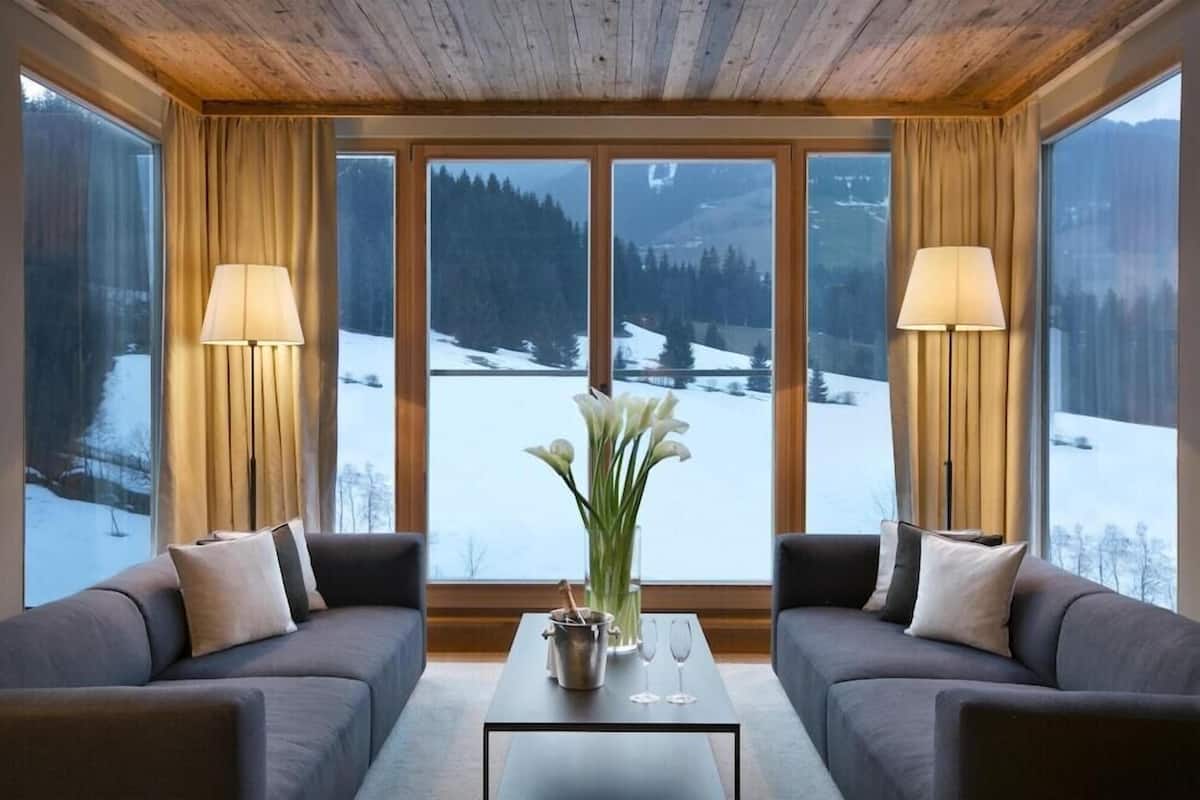 A cozy room with a sofa, a coffee table, and a view of a snowy landscape through large windows.