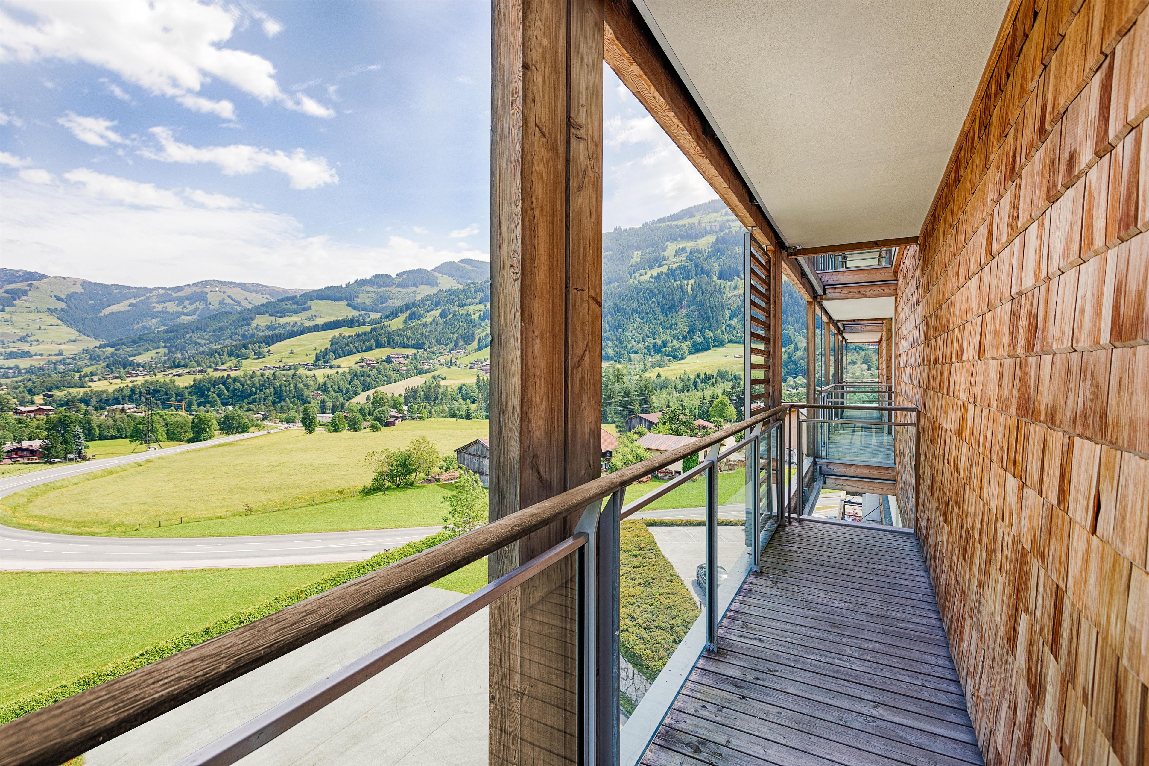 A wooden balcony with a glass railing overlooking a mountainous landscape.