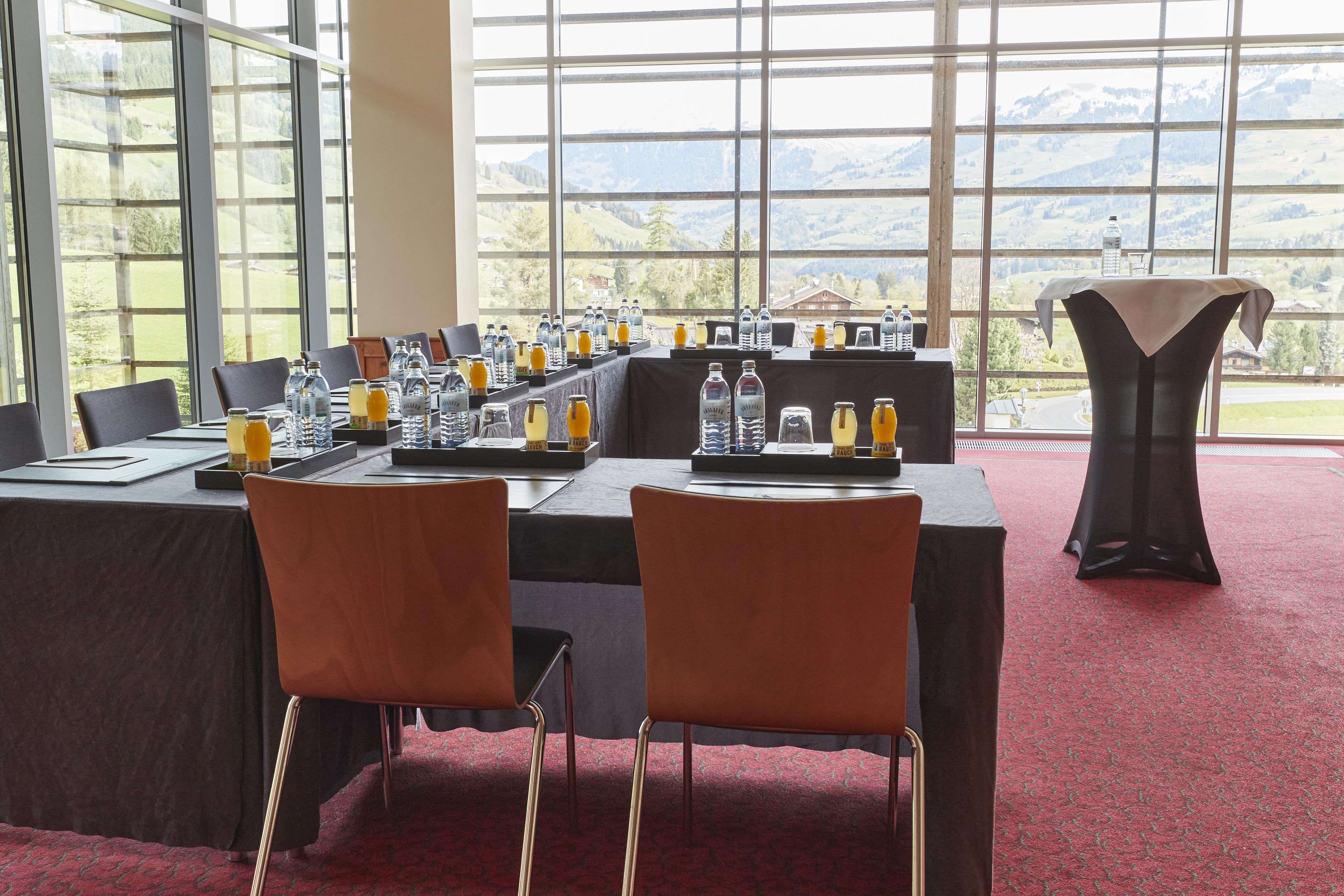 Sala de conferências com uma mesa comprida montada para uma reunião, cadeiras e vista de uma paisagem montanhosa através de grandes janelas.