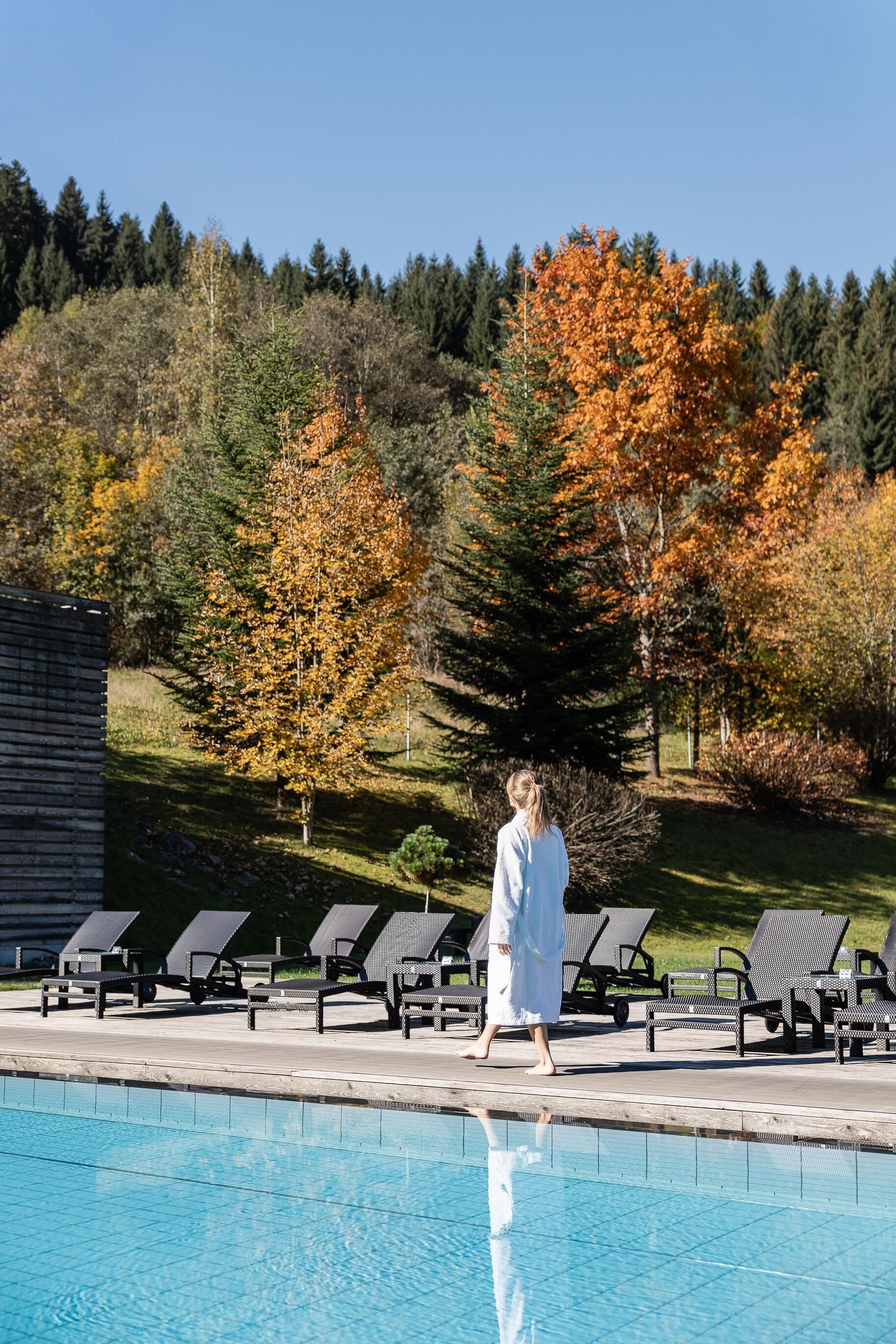 A pool area with lounge chairs and a person walking by.