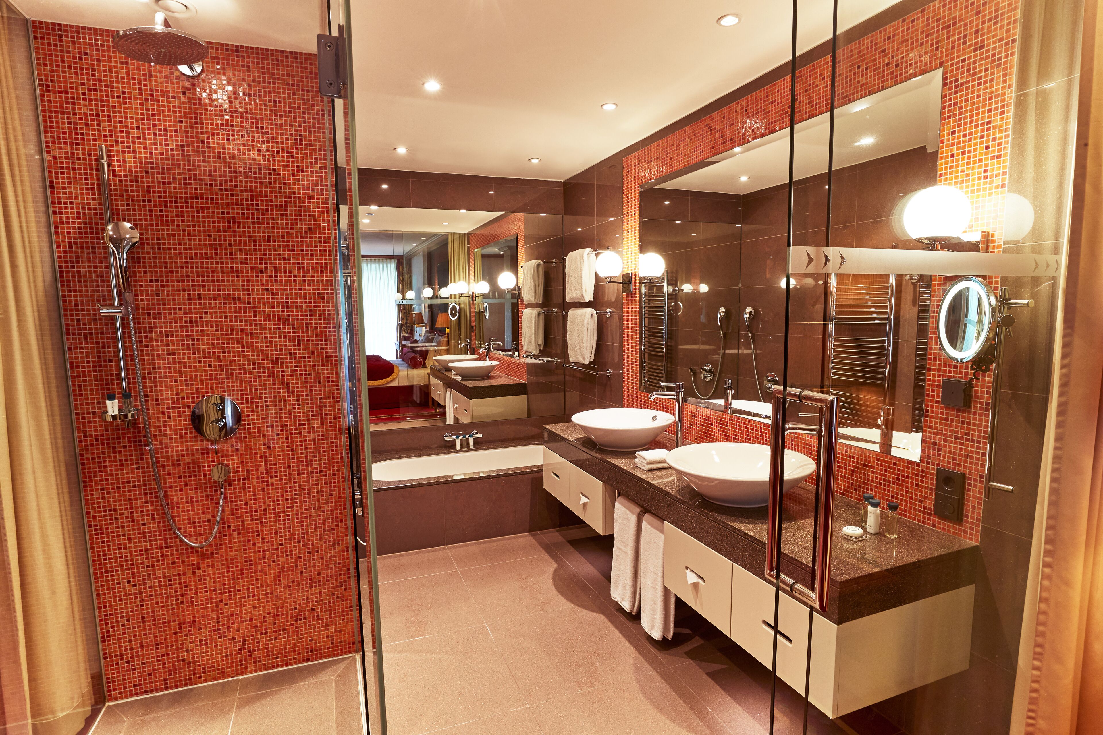 A modern bathroom with a glass-enclosed shower, two sinks, and a large mirror with lights.