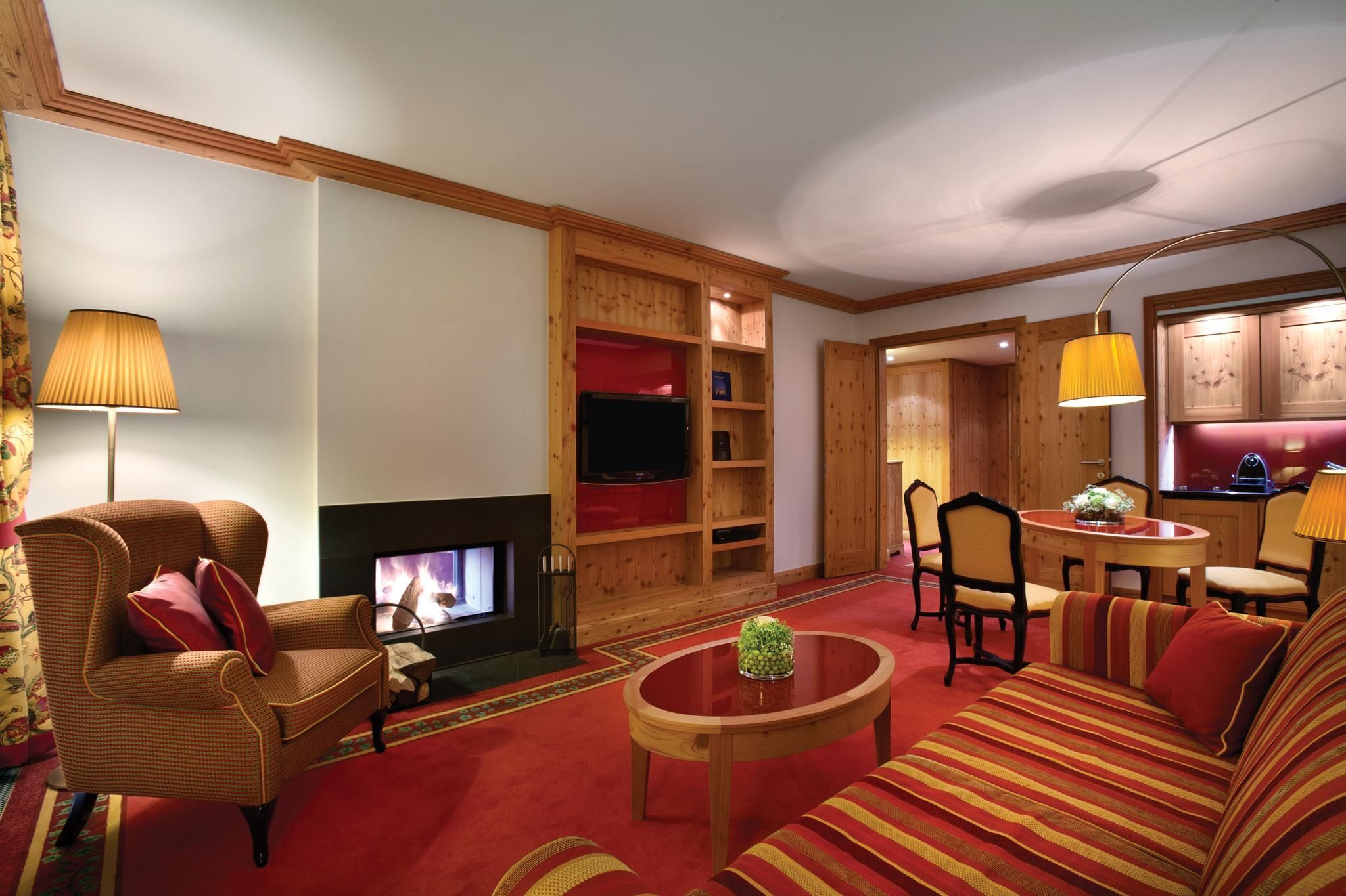 Una sala de estar con chimenea, un sofá, una silla, una mesa y una zona de cocina con armarios y una lámpara.