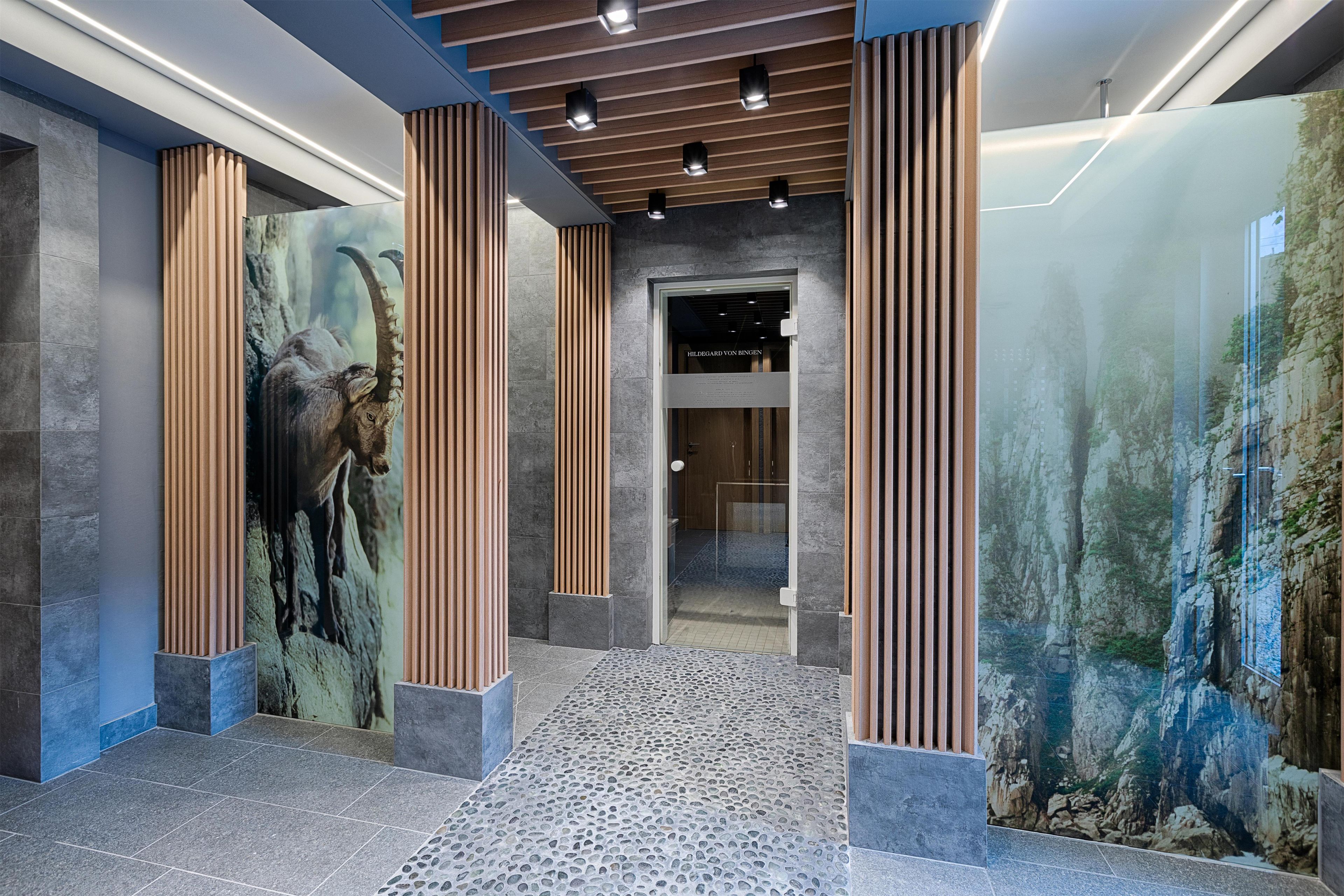 Un moderno vestíbulo con piso de piedra, columnas de madera y un mural grande en la pared.