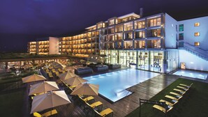 A modern hotel with a large outdoor pool, multiple balconies, and outdoor seating areas. - Kempinski Hotel Das Tirol (Jochberg)