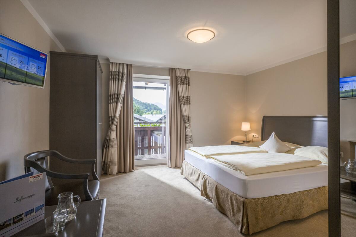 A hotel room with a bed, a desk, a chair, a TV, and a window with curtains.