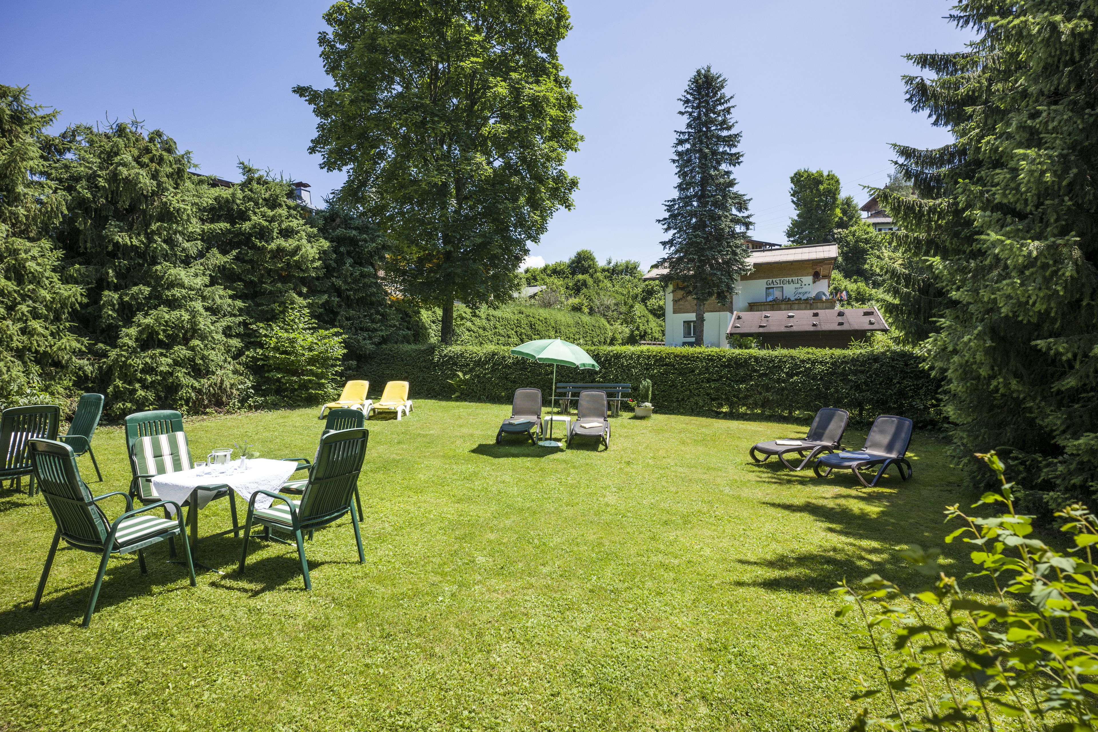 A well-maintained garden with a table and chairs, a lawn chair area, and a building in the background.