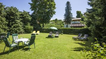 A well-maintained garden with a table and chairs, a lawn chair area, and a building in the background.