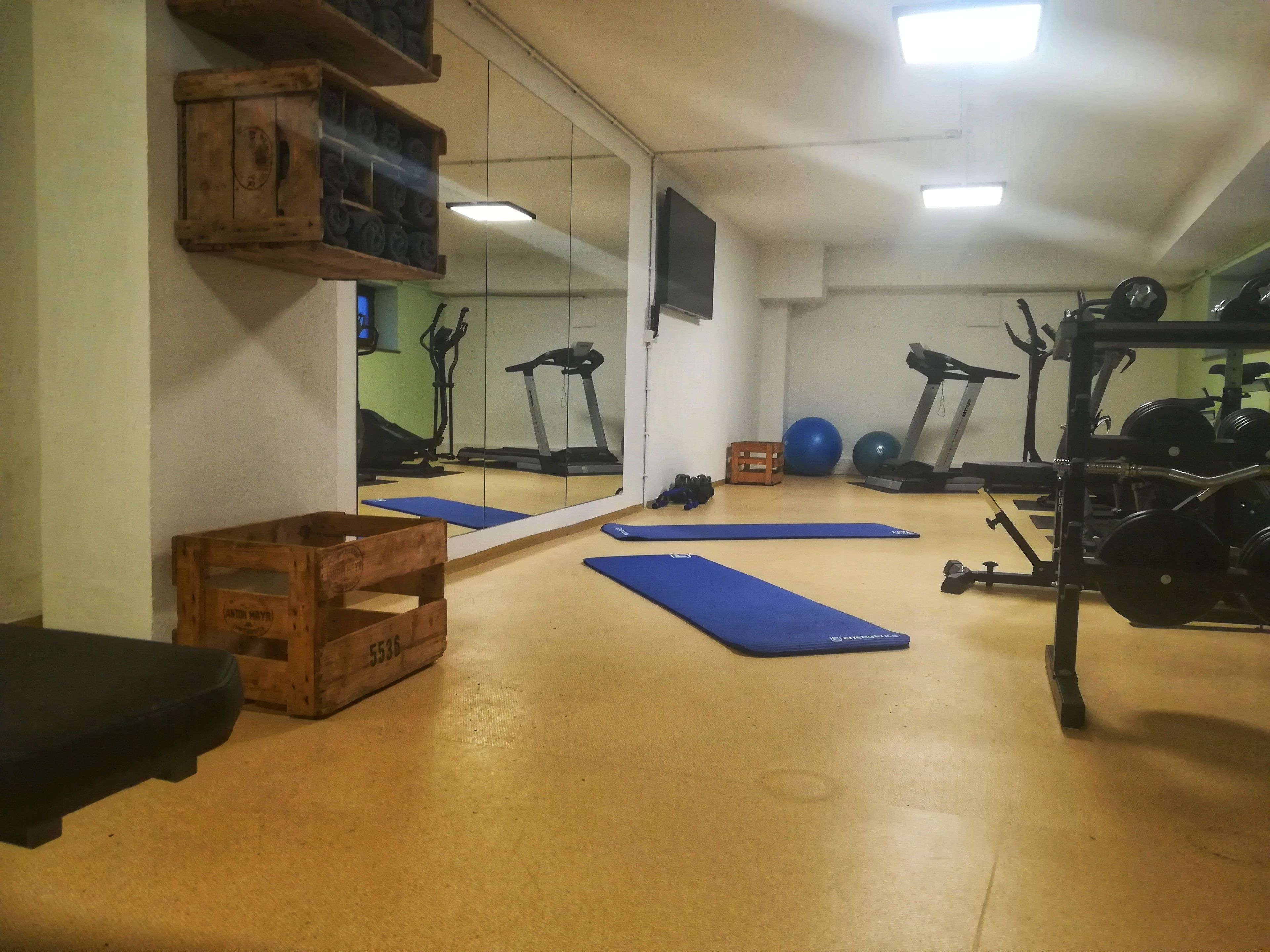 Un gimnasio con equipo de ejercicio, colchonetas y un espejo.