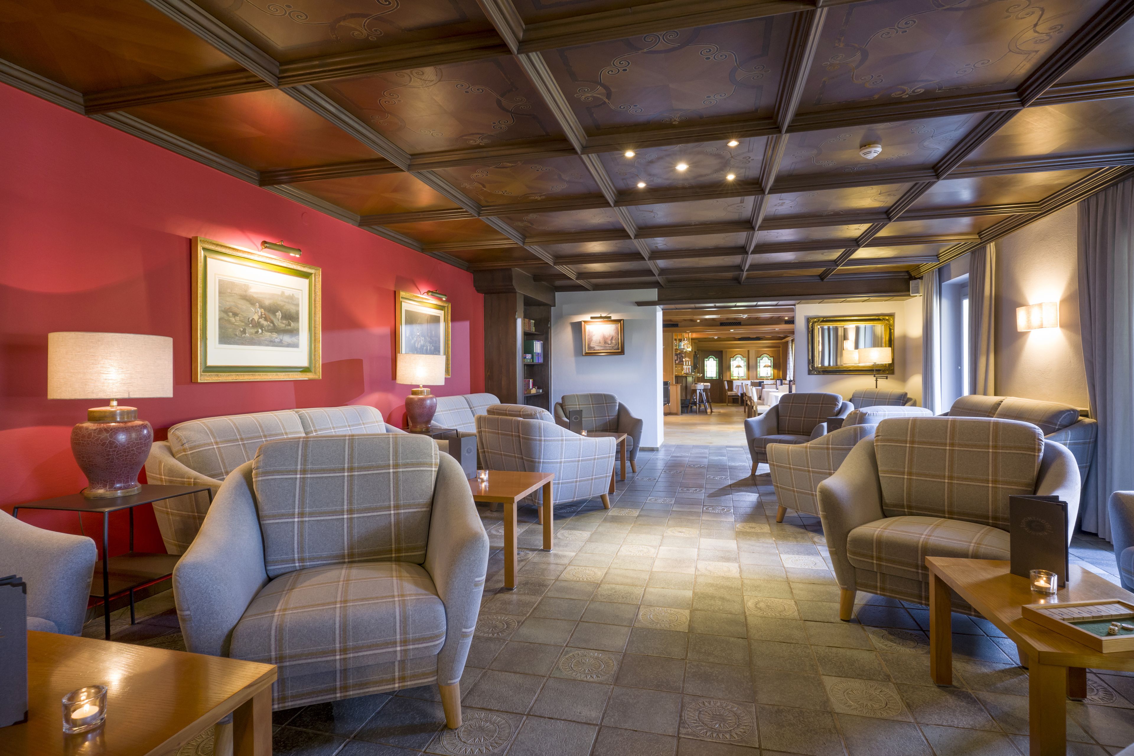 Un hall d’hôtel avec un mur rouge, plusieurs espaces aménagés avec des sièges et un plafond en bois.