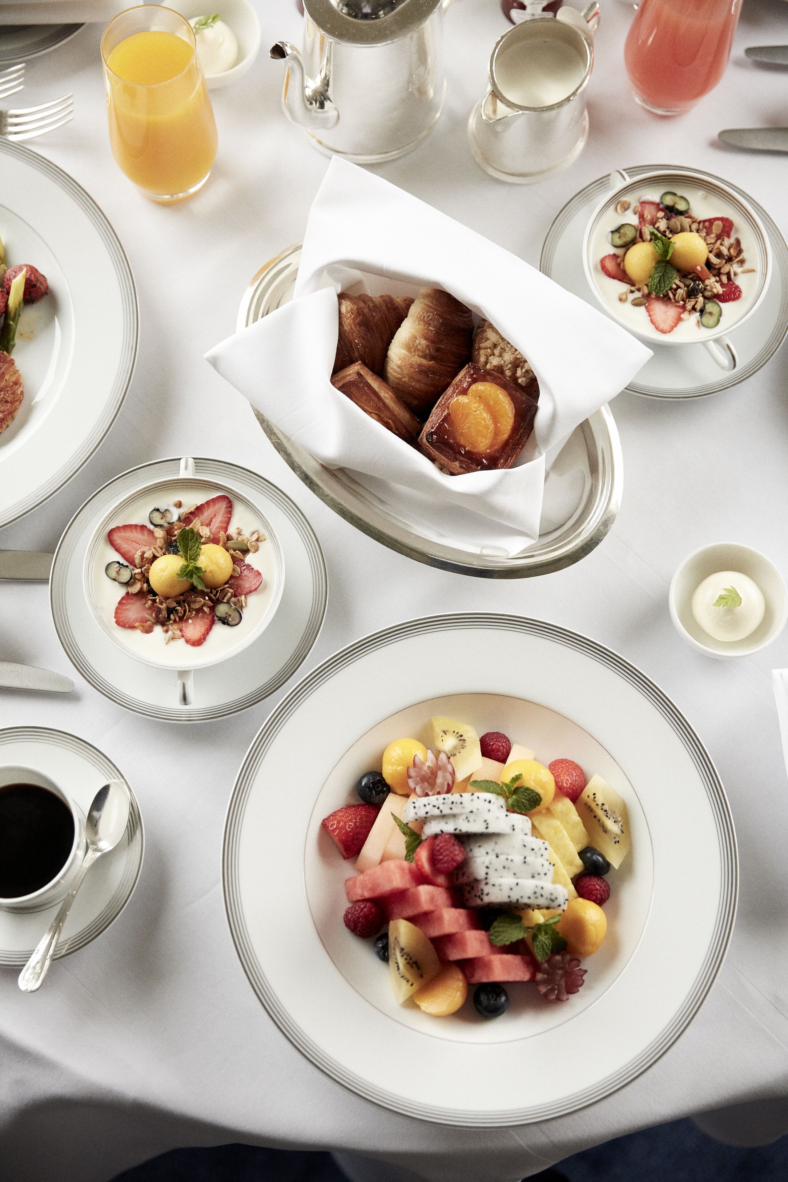 A breakfast setting with various dishes including fruit, yogurt, and pastries on a white table.