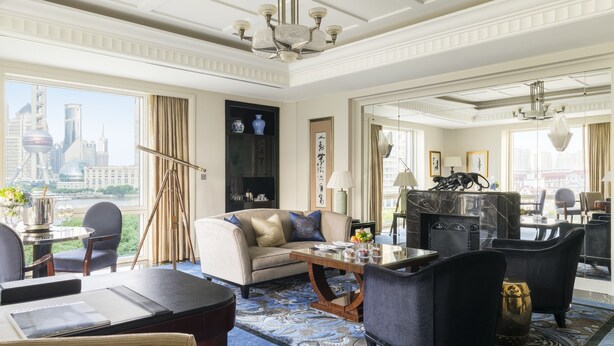 A spacious living room with a large window offering a city view, a fireplace, and a modern chandelier. - The Peninsula Shanghai (Shanghai)