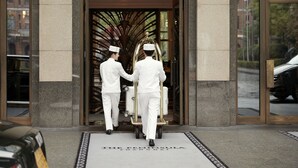 Two waiters in white uniforms pushing a cart with luggage through a hotel entrance. - The Peninsula Shanghai (Shanghai)