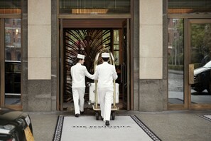 Two waiters in white uniforms pushing a cart with luggage through a hotel entrance.