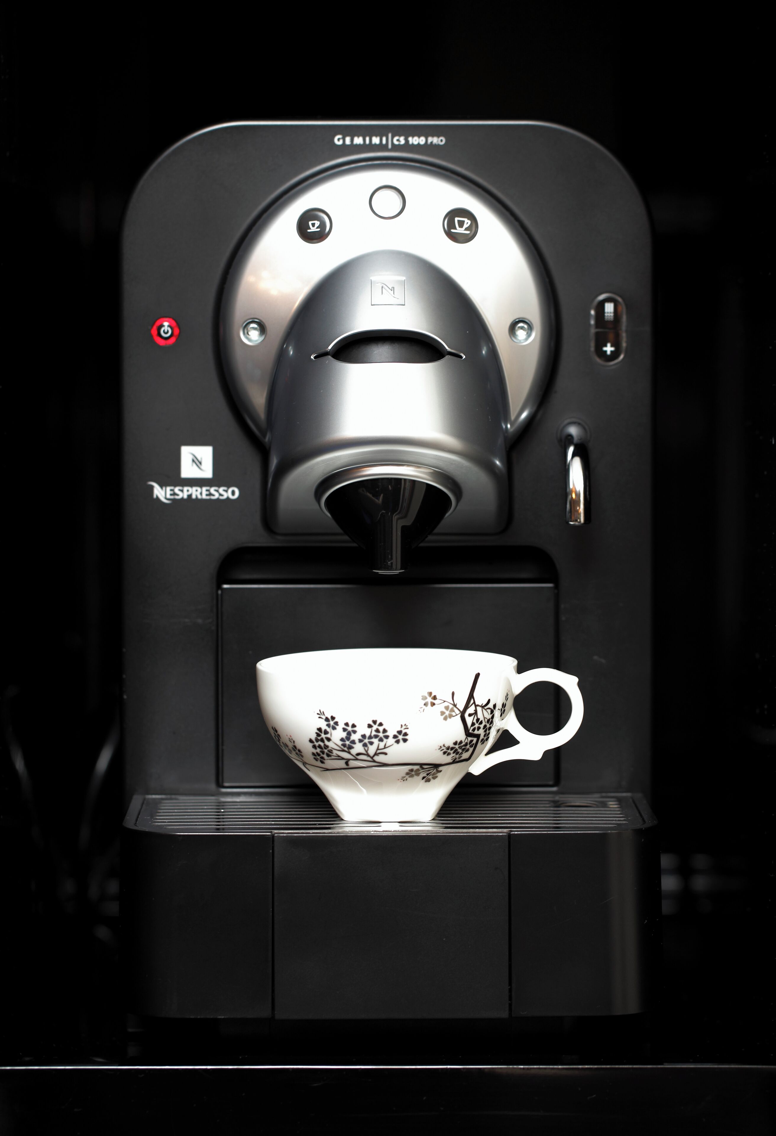A Nespresso Gemini CS 100 PRO coffee machine with a floral-patterned cup placed below it.