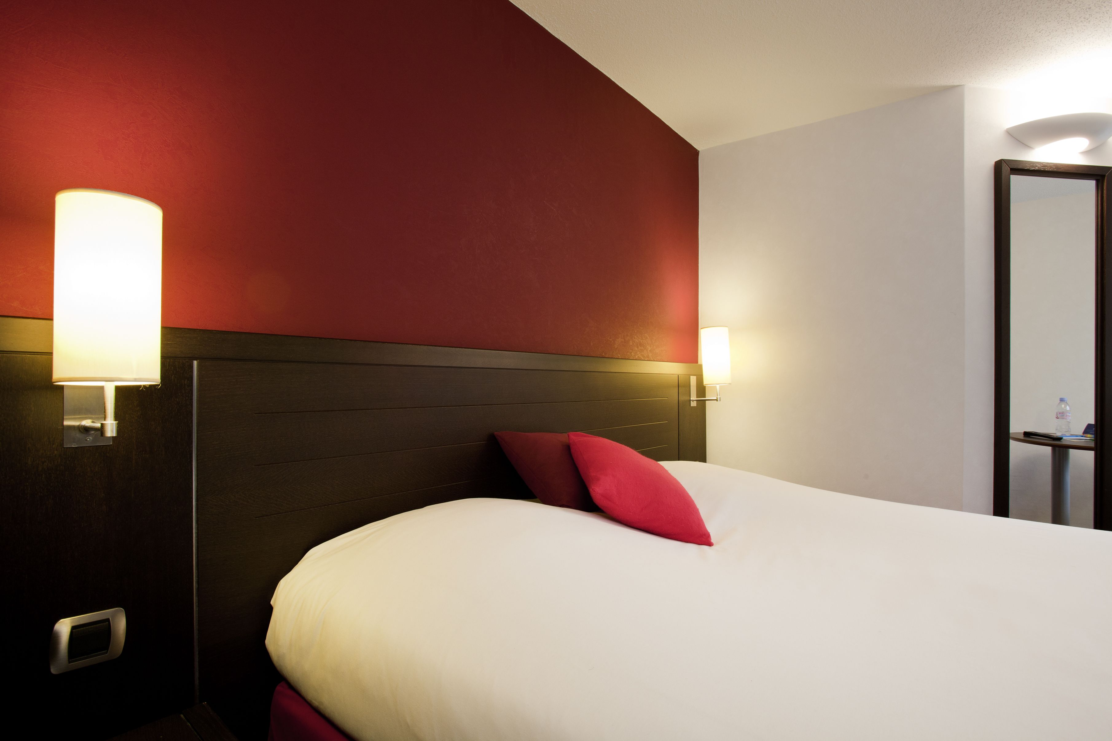 Ein Hotelzimmer mit einem großen Bett, roten Kissen und zwei Wandleuchten.