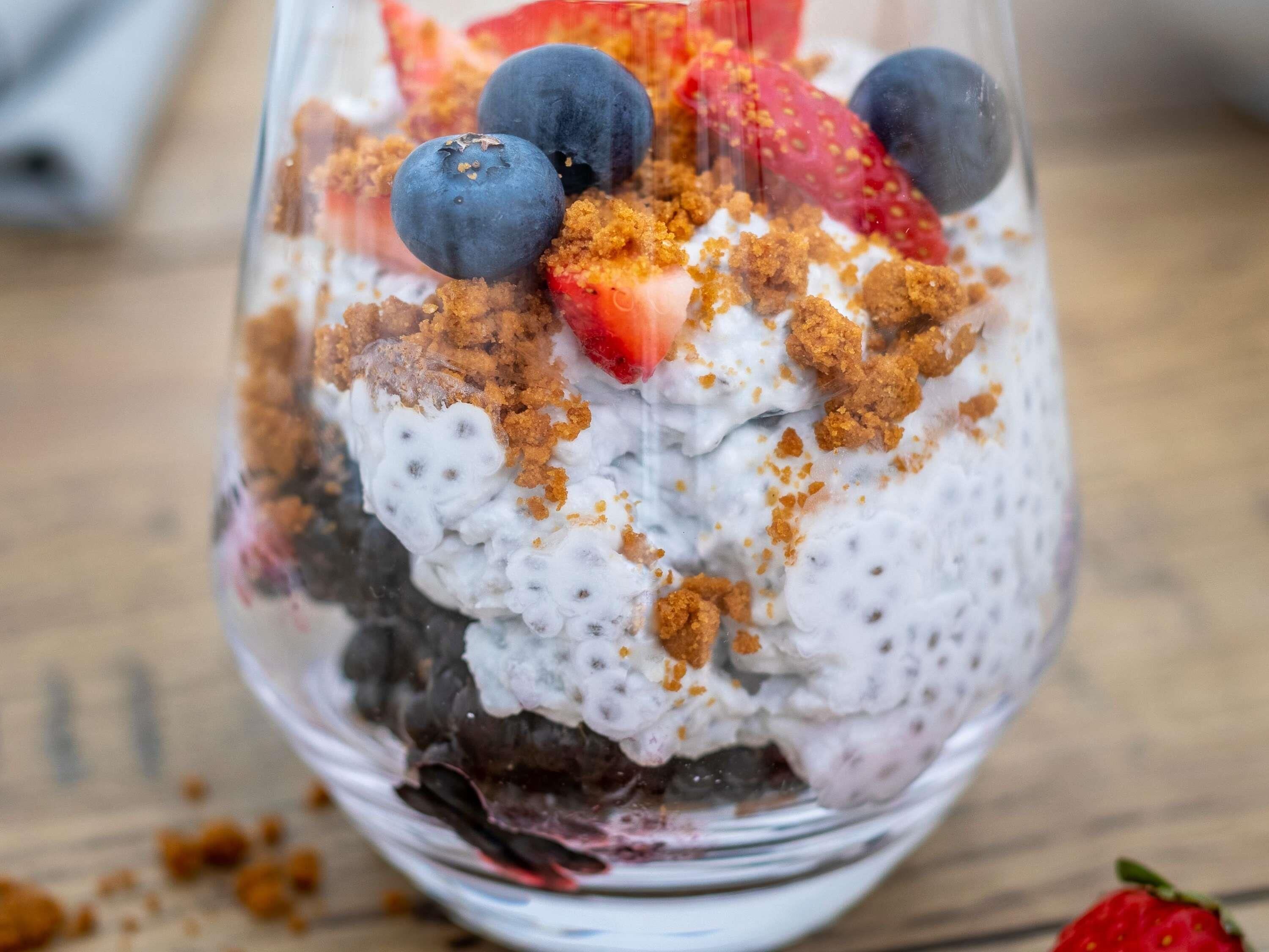 Postre en vaso transparente con fresas, arándanos y cobertura desmenuzada.