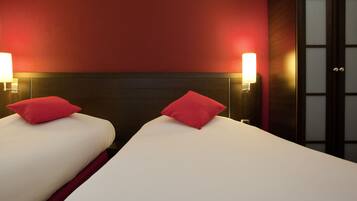 Ein Hotelzimmer mit zwei Betten, jedes mit einem roten Kopfkissen und einer Wandlampe.