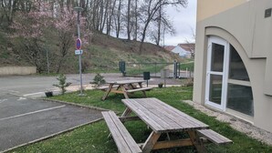 A parking area with picnic tables, a sign indicating a no parking zone, and a building with a large window. - Ibis Styles Belfort Centre (Belfort)