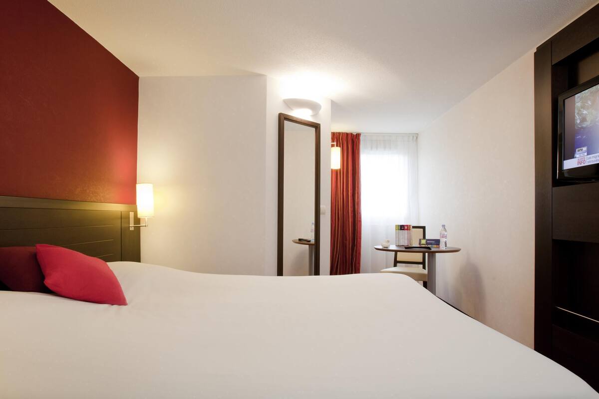 Une chambre d’hôtel avec un lit, un bureau, une chaise, une télévision et une porte.