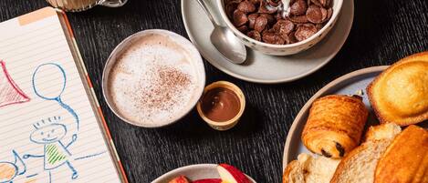 A breakfast setting with cereal, milk, a cup of coffee, croissants, fruit, and a notepad with a drawing.