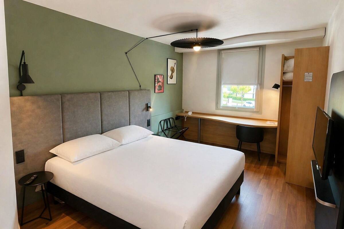 A bedroom with a bed, desk, chair, and a TV.