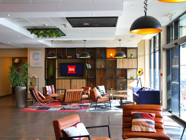 A modern lobby with seating, a TV, and a large window. - ibis Beauvais Aeroport (Beauvais)
