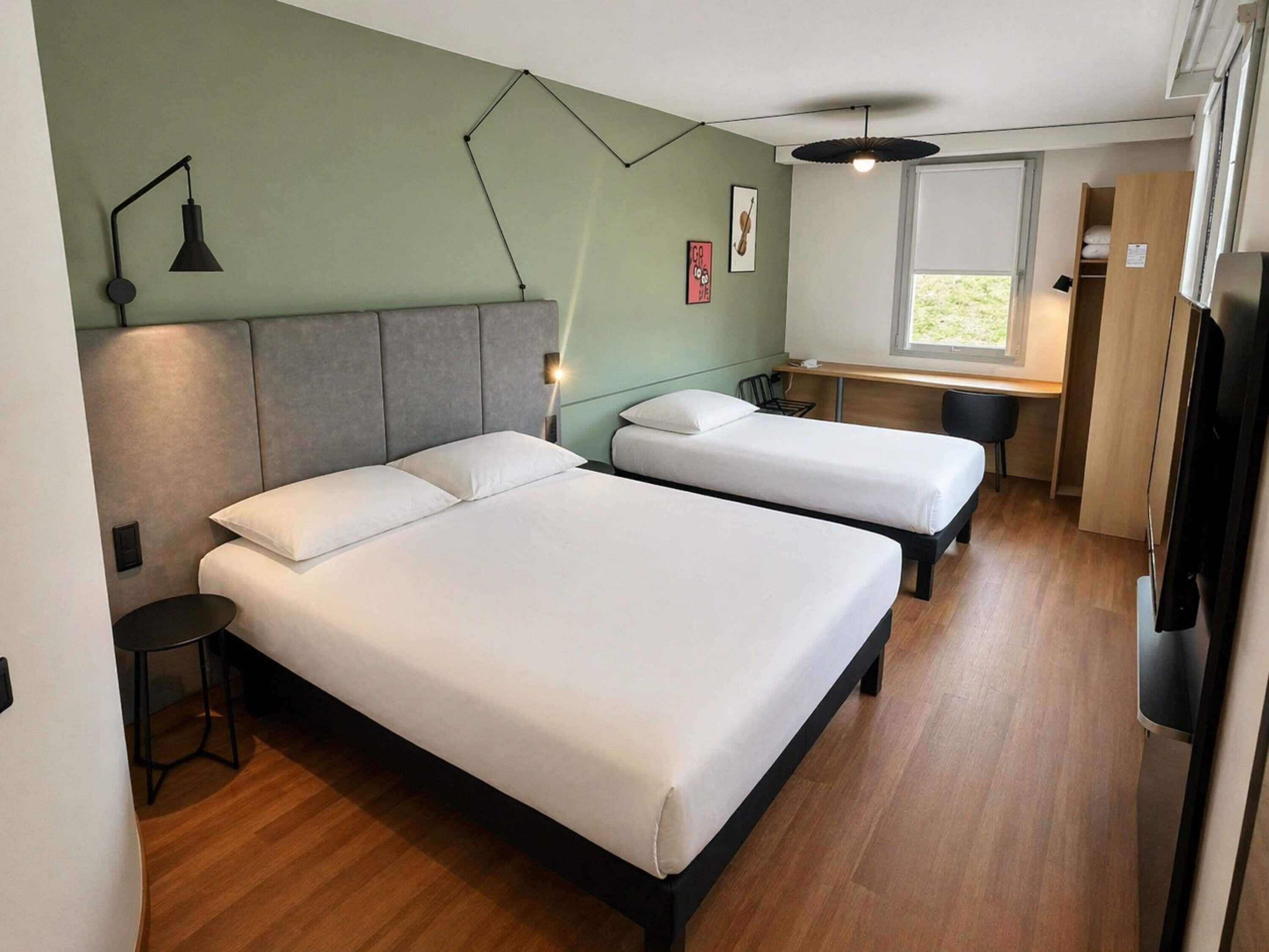 Ein Zimmer mit zwei Betten, einem Schreibtisch, einem Stuhl, einer Lampe und einem Fenster.