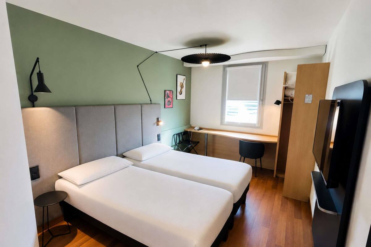 A room with two beds, a desk, a chair, a small table, a ceiling fan, and a TV.