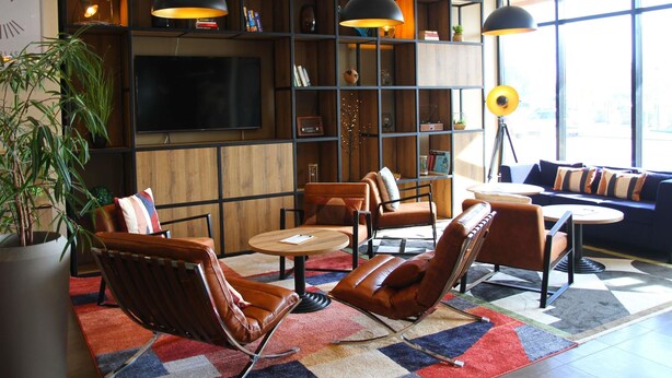 Una sala de estar moderna con sillones de cuero, una mesa redonda, una estantería y un televisor.