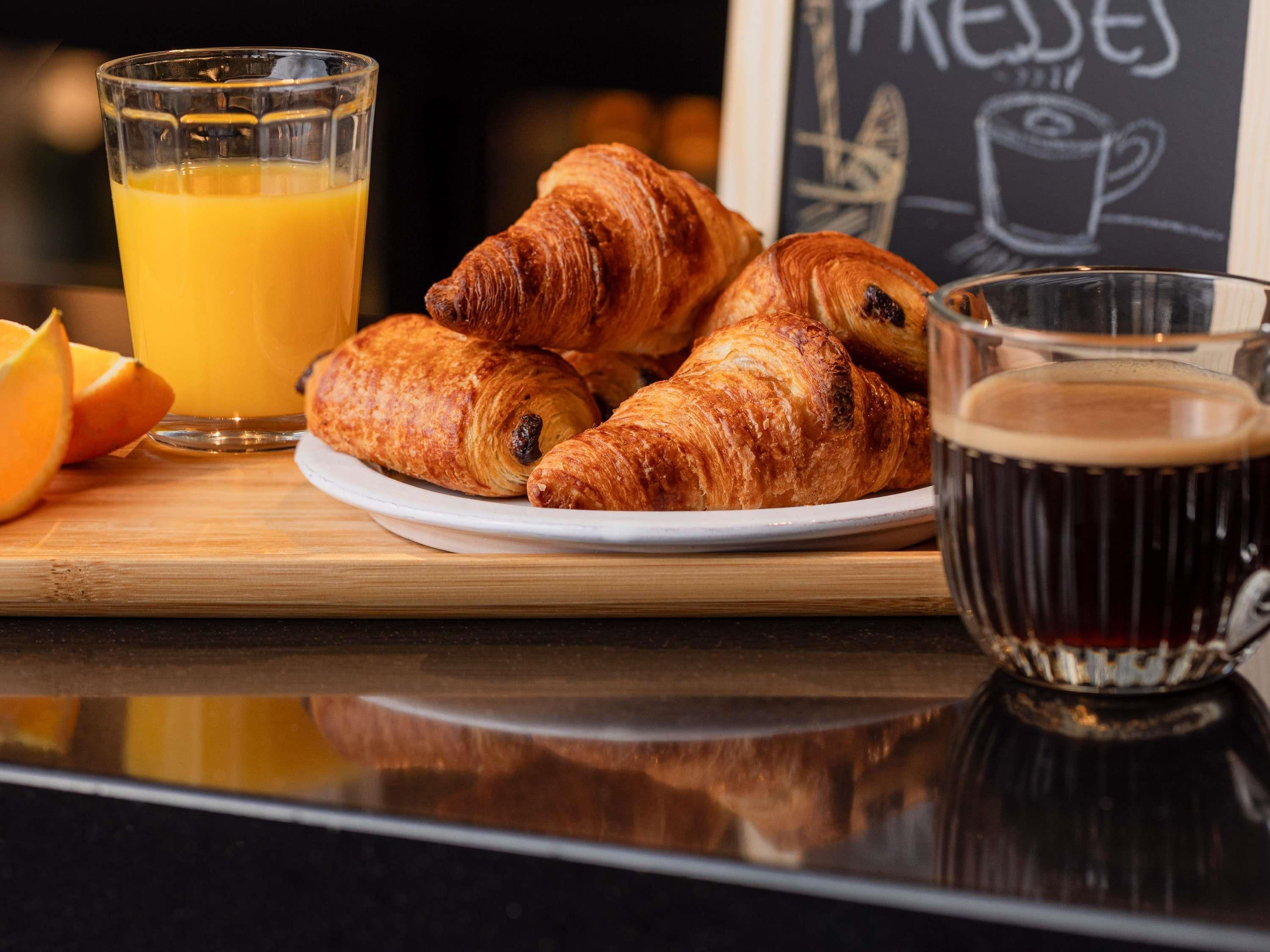 A breakfast setting with croissants, orange juice, and a coffee cup on a wooden table.
