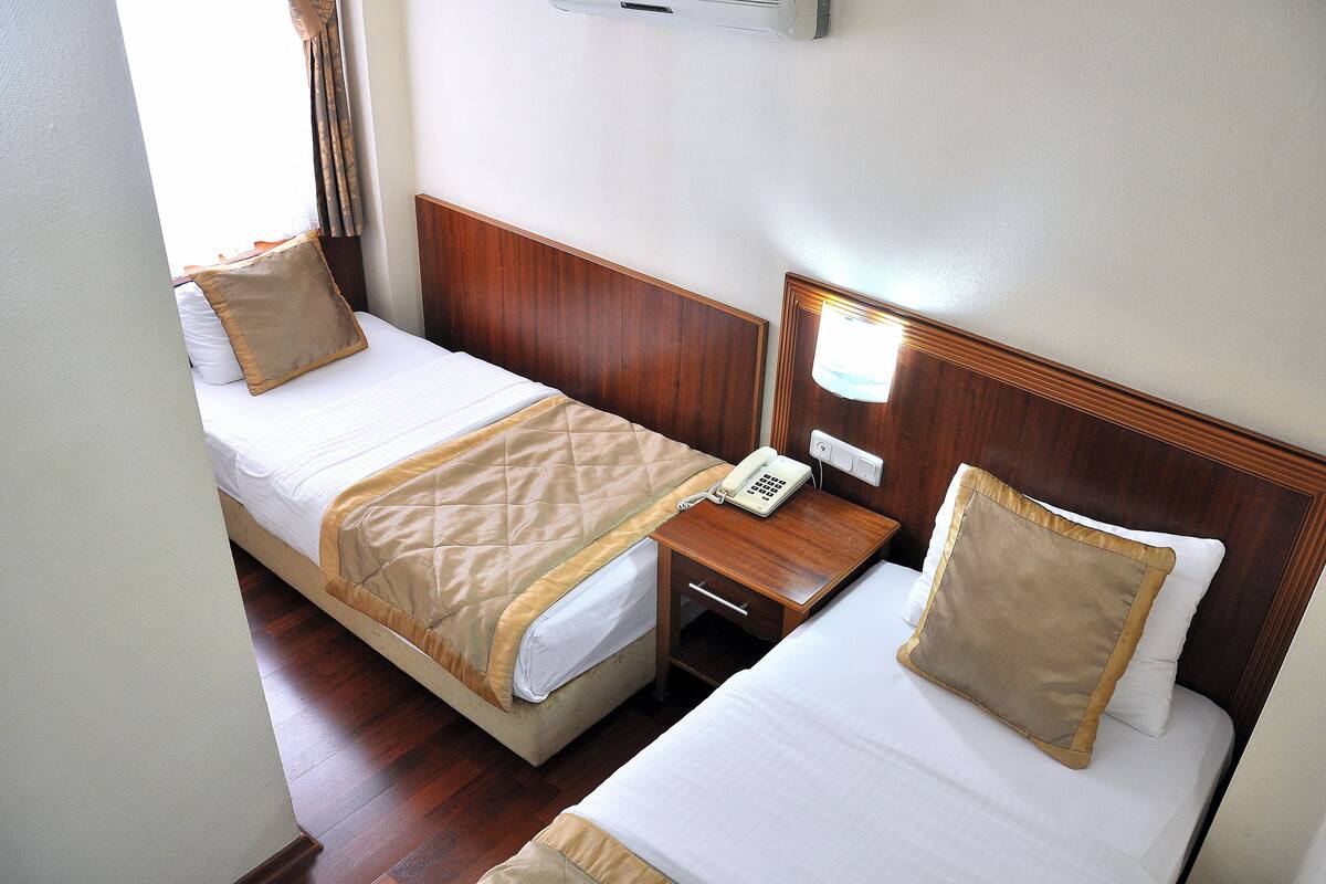 A hotel room with two beds, each with a wooden headboard, a bedside table with a lamp, and a phone.
