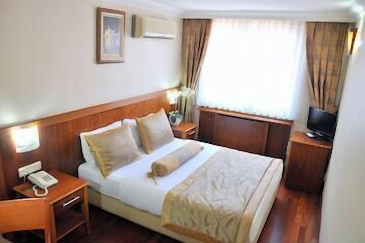 A hotel room with a bed, bedside tables, a TV, and a window with curtains.